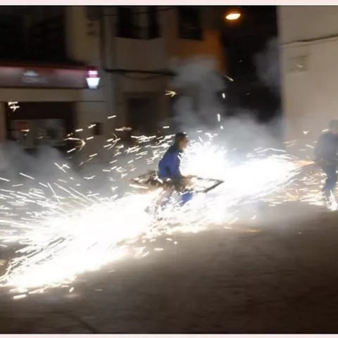 Chispas de pirotecnia iluminando una calle durante una celebración nocturna.