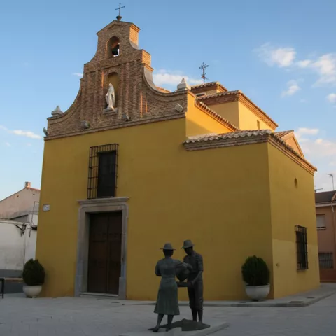 Fachada de una pequeña iglesia o ermita de color amarillo vibrante con una espadaña de ladrillo