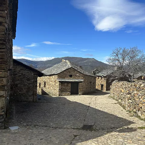 Conjunto de casas de piedra con montañas al fondo bajo cielo azul.