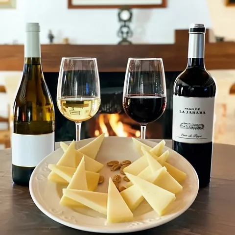 Botellas y copas de vino junto a un plato de queso, con chimenea encendida al fondo.