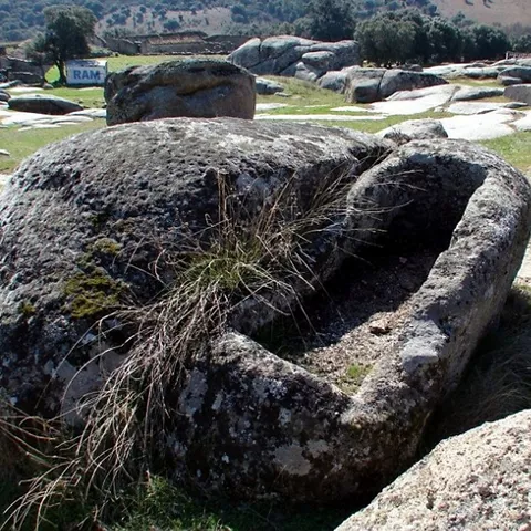 Tumba excavada en gran bloque de piedra con paisaje al fondo.