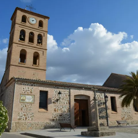Iglesia parroquial de piedra con torre campanario y palmera