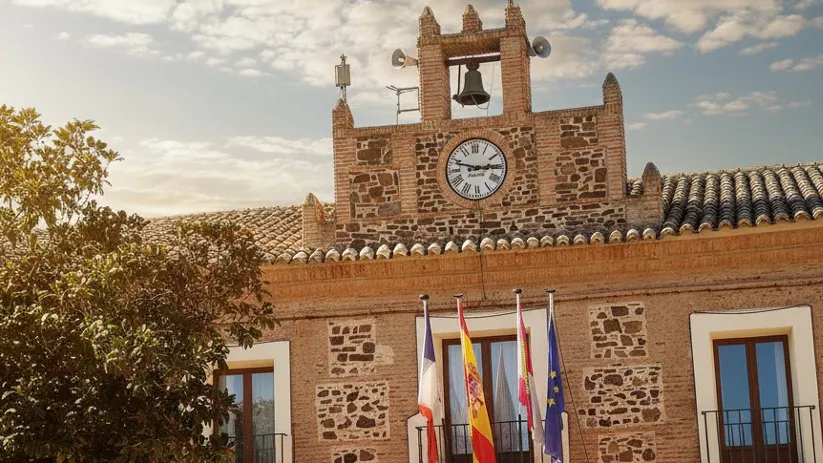Fachada del Ayuntamiento de Almuradiel con reloj y banderas oficiales en la plaza principal del municipio.