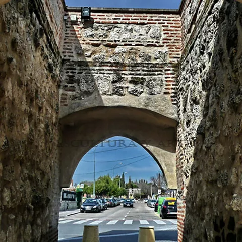 Vista interior del arco con calle y vehículos al fondo.