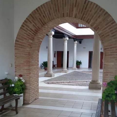 Galería porticada con columnas toscanas y balconada superior acristalada en un palacio histórico.