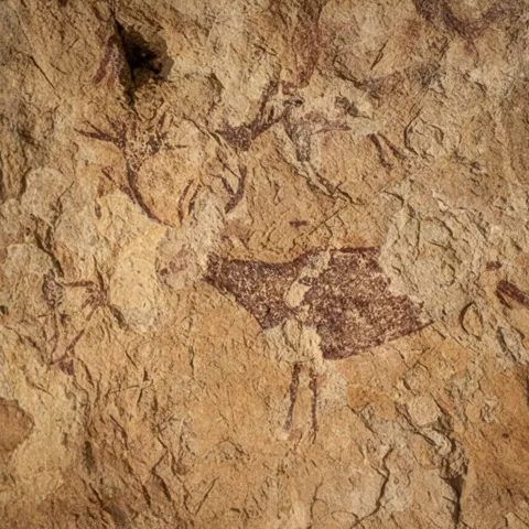 Figura de ciervo pintada en rojo sobre pared rocosa irregular.