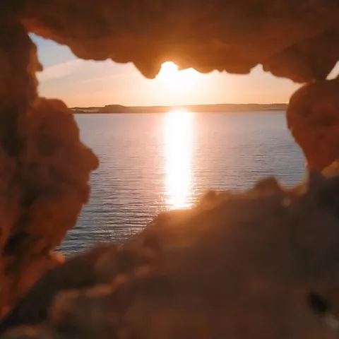 Puesta de sol sobre un embalse vista a través de una abertura en la roca.