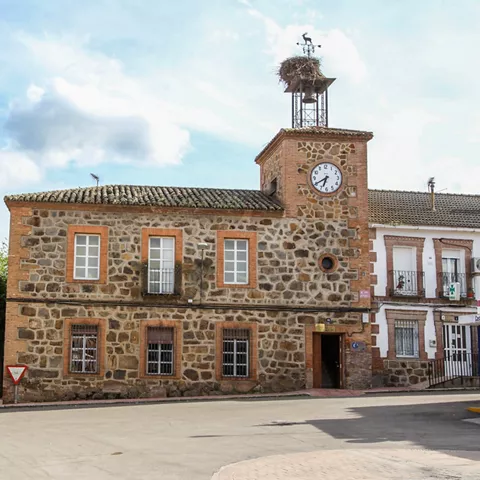 Edificio histórico de piedra con reloj en la fachada, situado en una plaza.