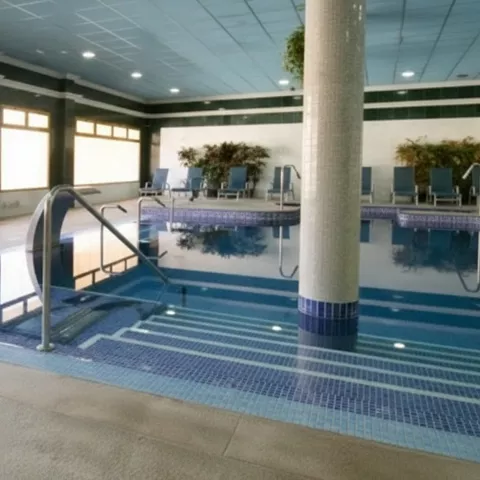 Zona de piscina climatizada con escalera metálica y ventanales grandes.
