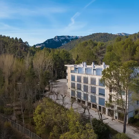 Edificio moderno junto a un valle arbolado, con montañas en el horizonte.