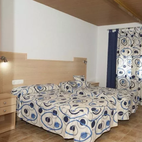 Habitación con dos camas, cortinas azules y televisor