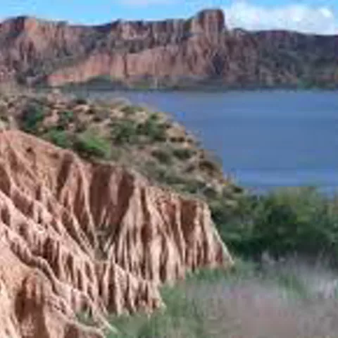 Formaciones erosionadas de roca rojiza junto a una masa de agua.