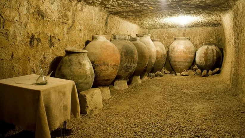Bodega subterránea con tinajas de barro alineadas.
