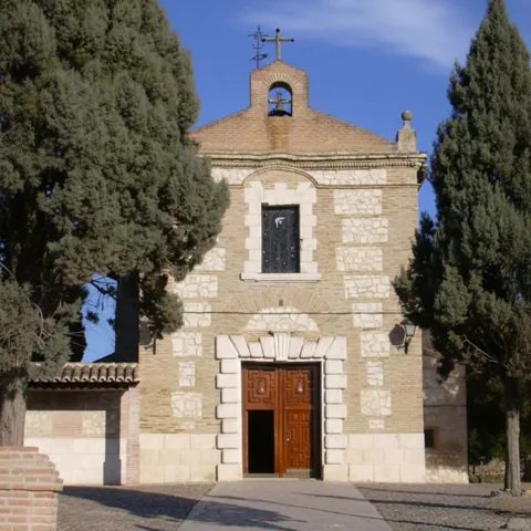 Ermita de piedra entre cipreses bajo cielo azul