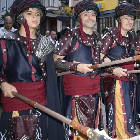Grupo de participantes con trajes oscuros y armas ceremoniales en formación