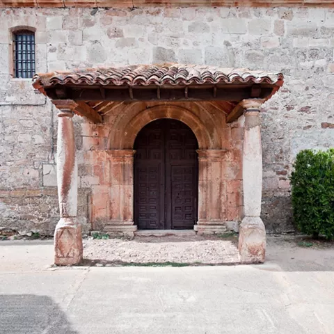 Portada románica de piedra con arco y columnas bajo un tejado de tejas.