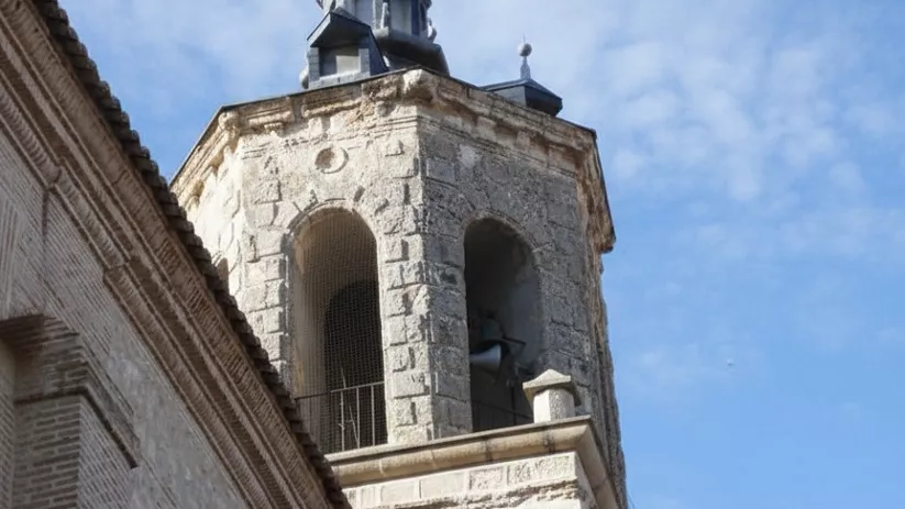 Campanario de piedra con espadaña y cruz visto en contrapicado