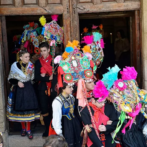 Grupo con trajes tradicionales saliendo de un edificio con varas decoradas.