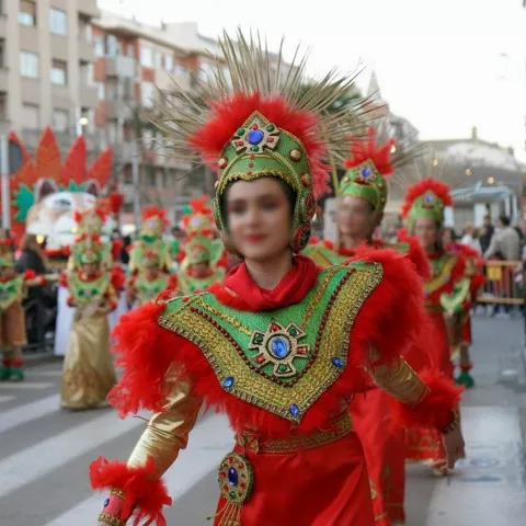 Persona con traje rojo y tocado ornamental desfilando en comparsa por la calle.