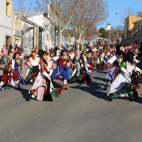Grupo de personas con trajes tradicionales desfilando y bailando por una calle urbana.