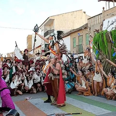 Grupo numeroso con vestuario festivo y plumas posando en plena calle durante el carnaval.
