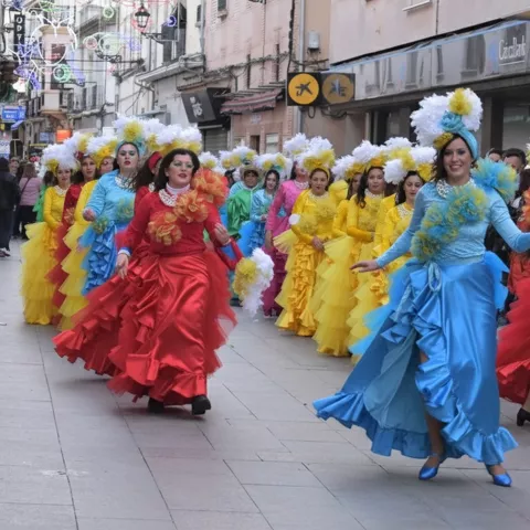 Comparsa con vestidos coloridos y tocados florales desfilando por la calle.