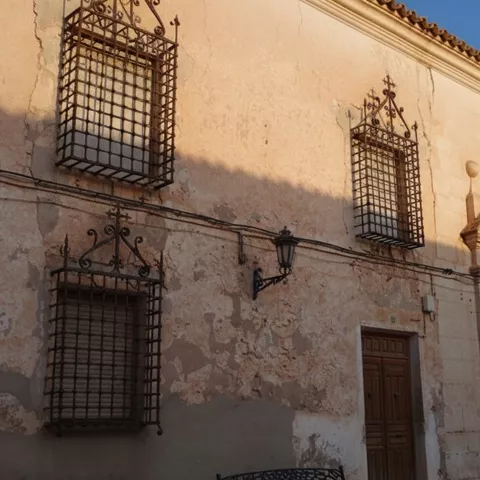 Fachada de edificio antiguo con rejas de hierro en las ventanas y puerta de madera.