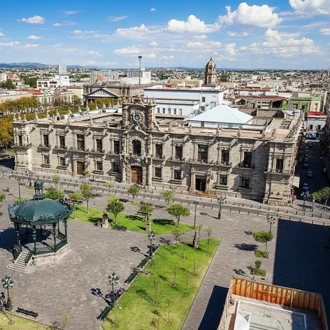Plaza histórica con quiosco de hierro y palacio de piedra.