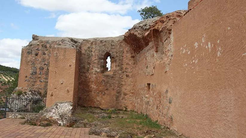 Ruinas de un edificio histórico de piedra con muros parcialmente derruidos y pequeñas ventanas arqueadas, bajo un cielo azul con nubes.
