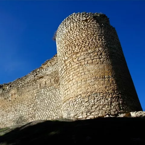 Torre circular y lienzo de muralla iluminados por el sol.