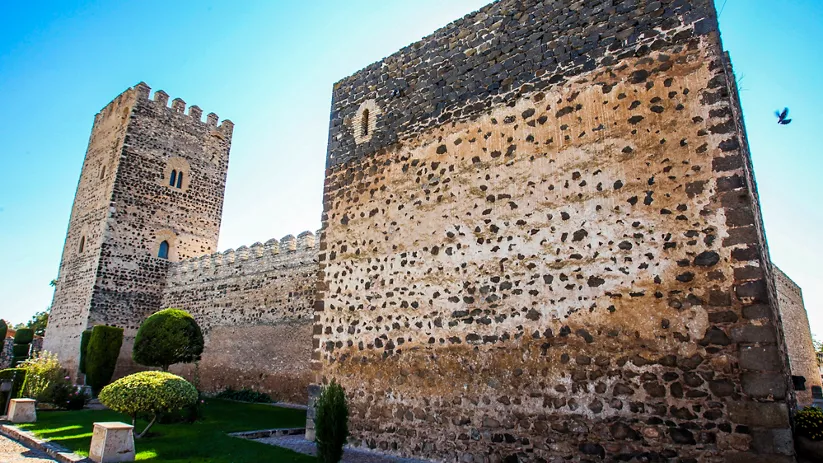 Torre y lienzo de muralla del castillo medieval bajo cielo azul.