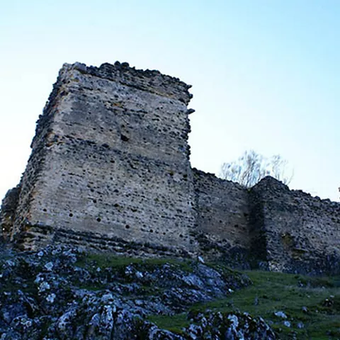Torre de piedra en ruinas sobre un terreno rocoso y verde..