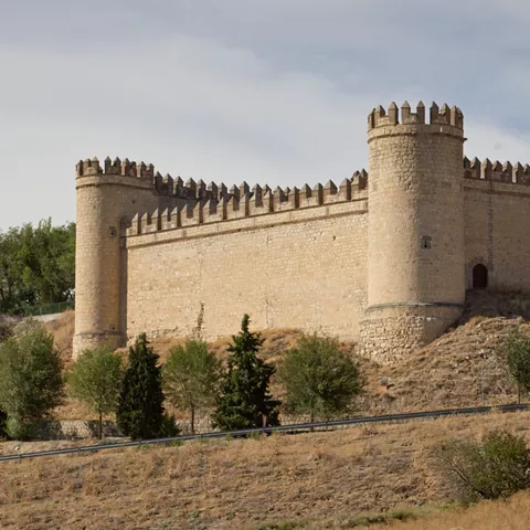 Castillo medieval de piedra iluminado por el sol en lo alto de un cerro.