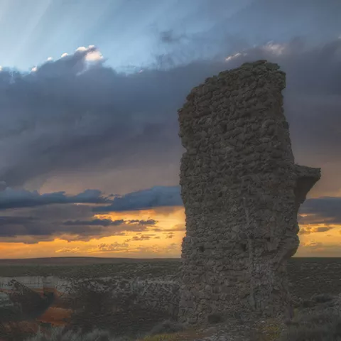 Torre de piedra en lo alto de un cerro al atardecer con cielo tormentoso.
