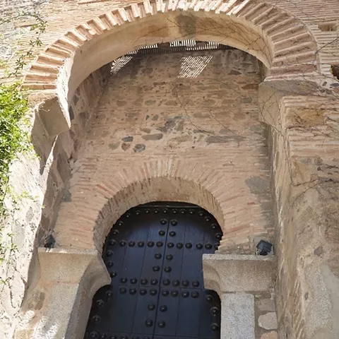 Puerta de acceso con arco de ladrillo y portón de madera reforzado con clavos.
