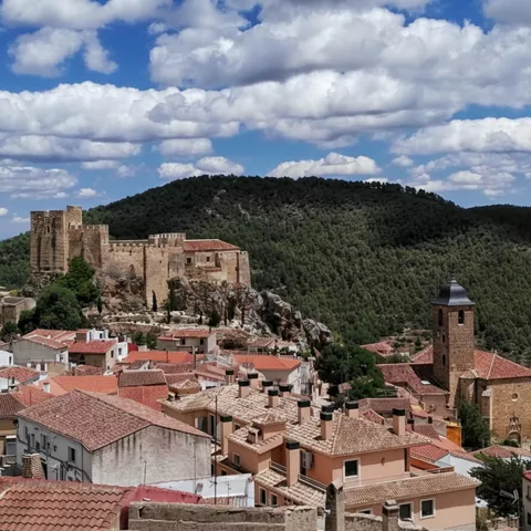 Panorámica de pueblo con iglesia y castillo en lo alto de la montaña.