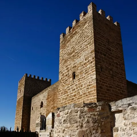 Torre almenada junto a muro de piedra y patio empedrado.