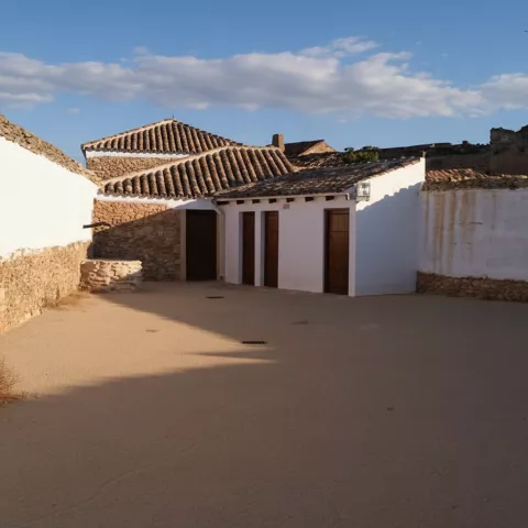 Patio amplio de muros blancos y piedra, con puertas de madera y tejado de teja.
