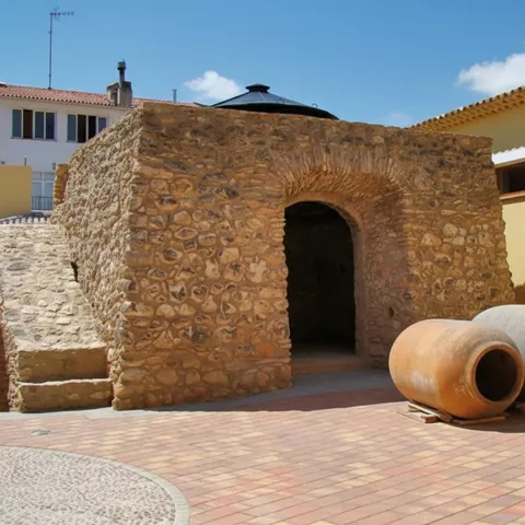 Plaza con construcción de piedra y tinajas de barro apoyadas junto a un muro amarillo.