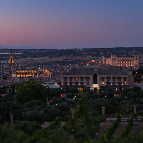 Vista nocturna de la ciudad con edificios iluminados y colinas oscuras.