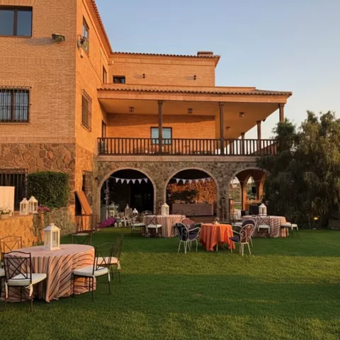Jardín con mesas redondas junto a edificio de ladrillo al atardecer.