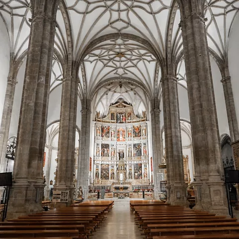 Nave de iglesia con altas columnas, bóvedas góticas y retablo mayor