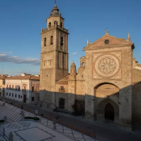 Iglesia monumental con torre y rosetón iluminada por luz cálida de la tarde.