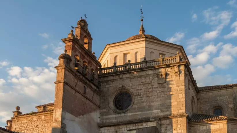 Fachada de piedra con torre y cúpula, vista desde abajo con cielo azul.