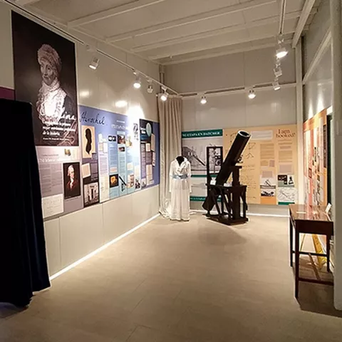 Pasillo museístico con paneles explicativos y telescopio antiguo en exhibición.