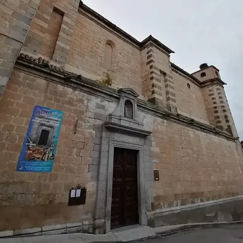Fachada lateral de iglesia de piedra con portada y cartel conmemorativo.