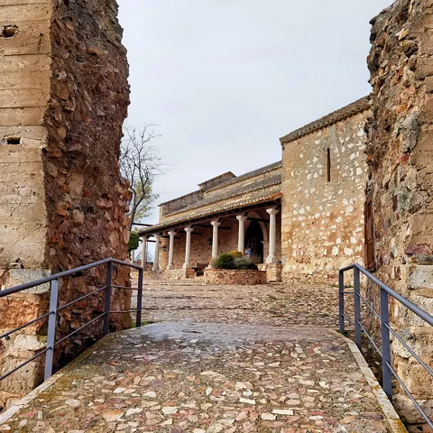 Acceso empedrado entre muros de piedra hacia un edificio histórico.