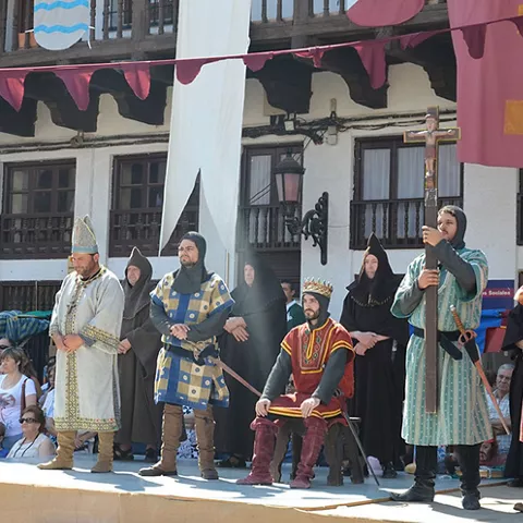 Desfile histórico por una calle con participantes portando estandartes y escudos.