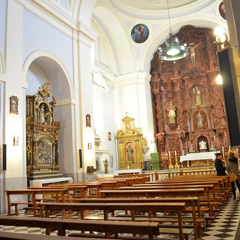 Interior de iglesia con bancos y retablo barroco.