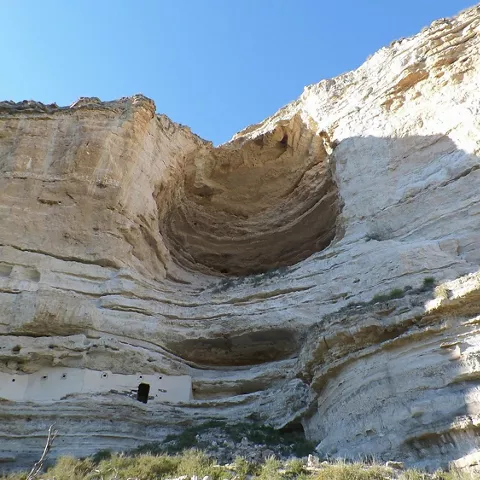 Gran oquedad en acantilado calcáreo vista desde la base con cielo azul.